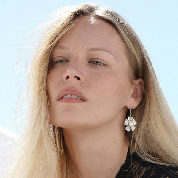 Close up on a face of a blonde model wearing silver flower earrings.