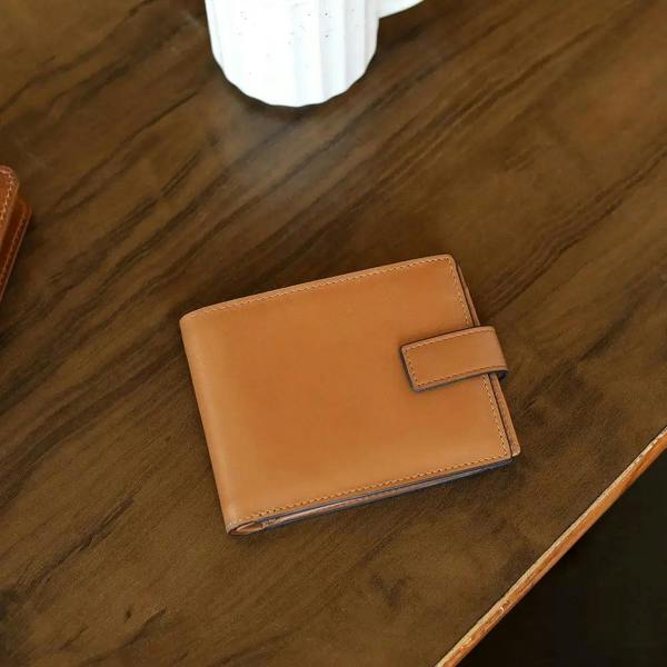 Tan leather wallet on a wooden surface with a white mug in the background