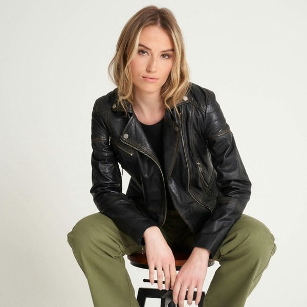 Image displays a model sat on a stool modelling the washed clara jacket from Barneys Originals. The jacket is black with a tan worn washed finish.