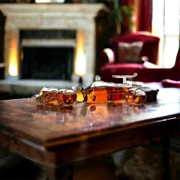 A glass racing car decanter filled with amber whisky sitting on a rustic wooden coffee table in front of a warm fireplace.