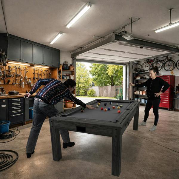 7-in-1 grey games table with a sleek design, featuring a billiards setup, darts, and LED lights, set in a garage environment