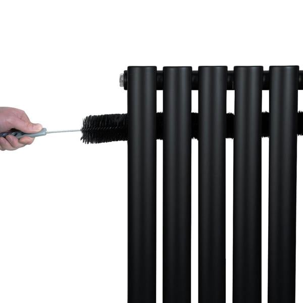 Black oval single column radiator with smooth, matte finish, featuring six vertical tubes and a hand cleaning brush in use