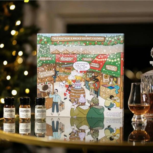That Boutique-y Whisky Company Advent Calendar box on a dark surface next to three wax-sealed miniature bottles and a poured glencairn glass.