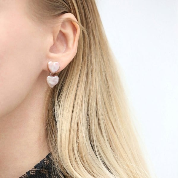 A close up of an ear with heart shaped pearl ear jacket earrings.