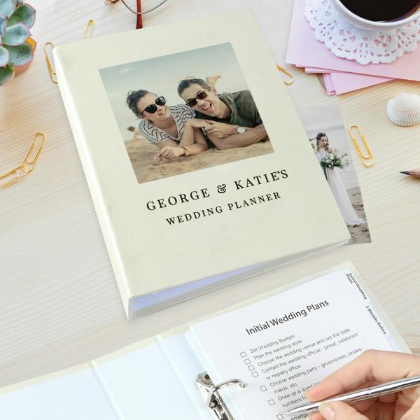 A personalised photo wedding planner book printed with George and Katie's Wedding Planner open on a desk with a checklist.