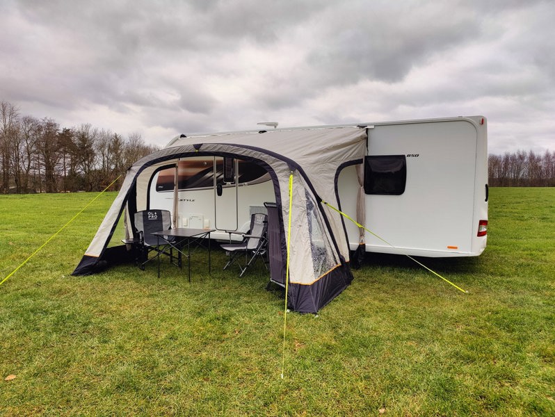 The OLPRO View Lite Breeze 390 Caravan Awning pictured in a Caravan site attached to a caravan with  some camping furniture on display inside of the awning.