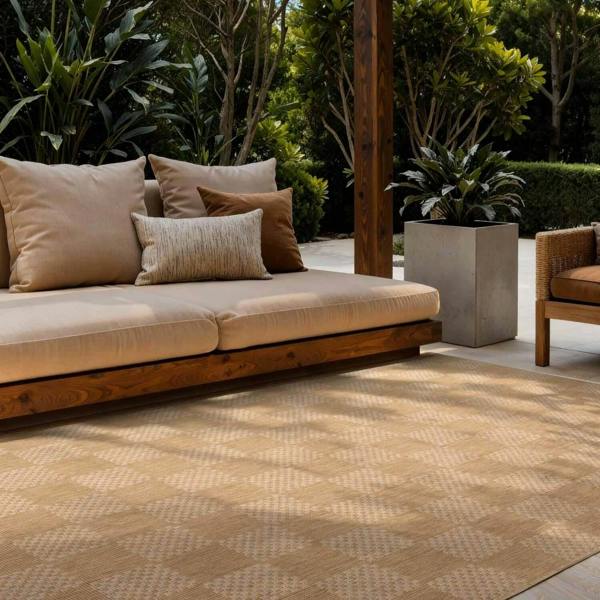 Outdoor seating area with a beige sofa and cushions on a patterned rug, surrounded by greenery.