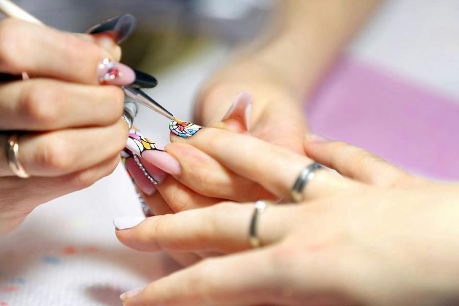 nail technician using nail brush to paint nail art designs on clients nails