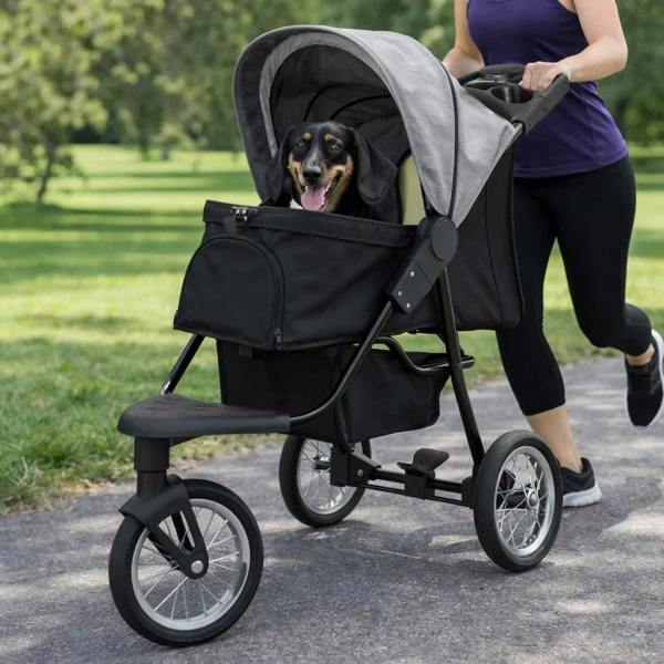 Grey pet jogger with a spacious canopy, black storage basket, and a happy dog inside, set on a park path with greenery in the background