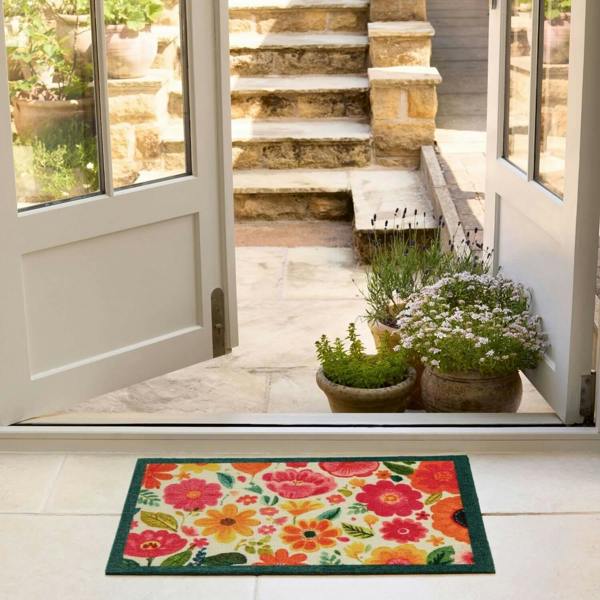Floral doormat in front of a house with plants and steps visible