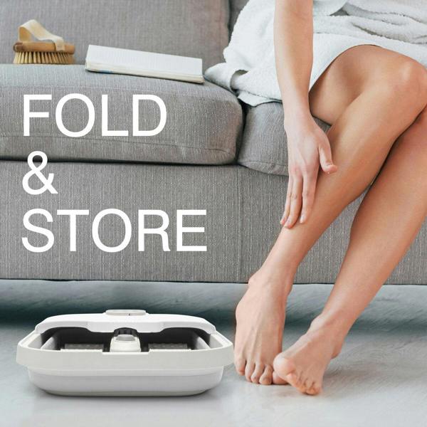 A person relaxes on a gray sofa, touching their leg beside the Deluxe Foldaway Foot Spa Bath by Rio, folded neatly on the floor. The words FOLD & STORE are displayed on the left side of the image.