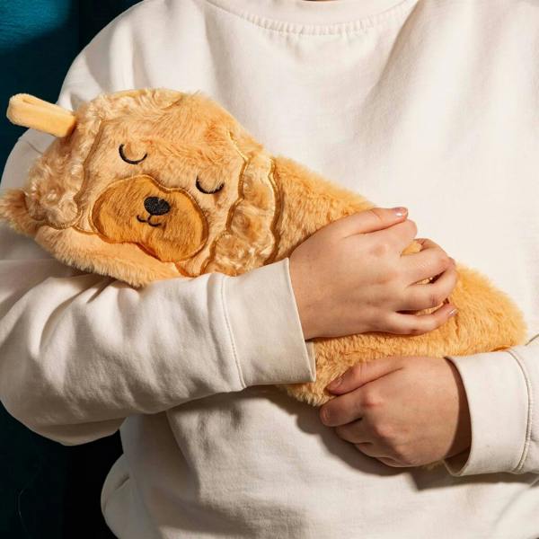 Person in a cream sweatshirt holding a soft plush honey-coloured cockapoo hot water bottle close.