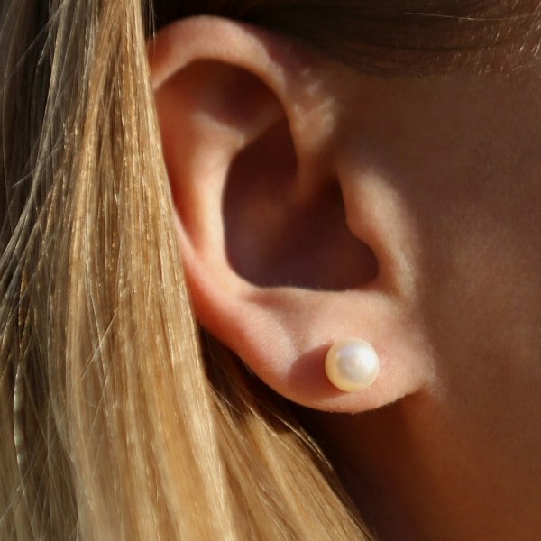 Close up of an ear with classic pearl studs.