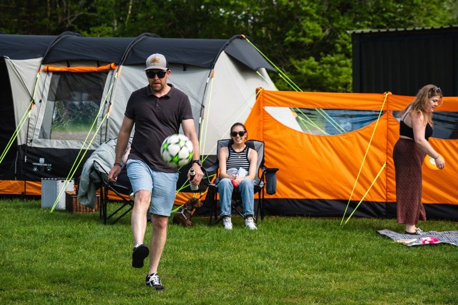 A party takes place outside of the Wichenford 8.0, an OLPRO inflatable windbreak is also in shot. People sit in the background whilst a man plays football