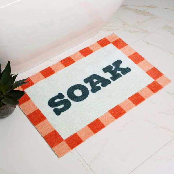 Doormat with 'SOAK' text on a checkered border in a bathroom setting