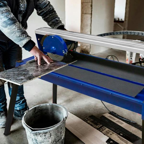 Wet tile cutter bench in blue with a 720mm blade, cutting a large dark marble tile, featuring a sturdy metal frame and water reservoir