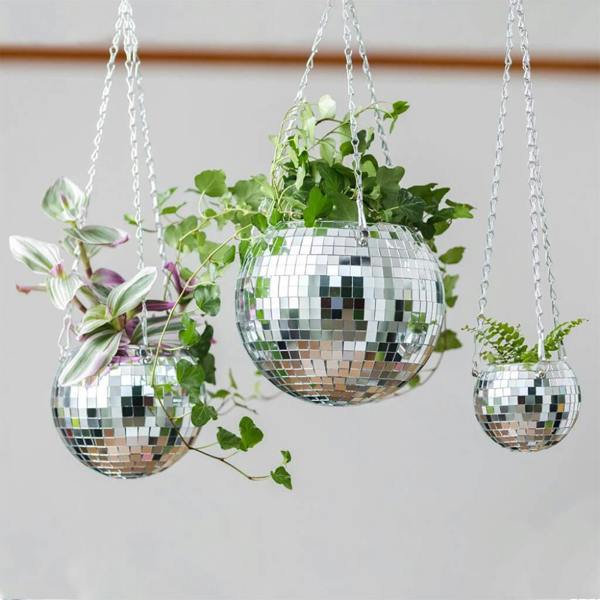 Three spherical hanging planters made of small, reflective mirrored tiles, each holding different lush green indoor plants, suspended from a ceiling by silver chains.