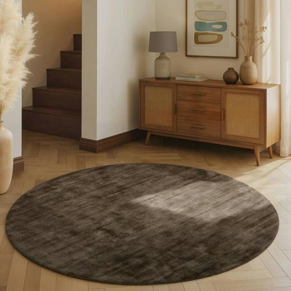 Round gray rug on a wooden floor with a wooden cabinet and decorative items in the background.
