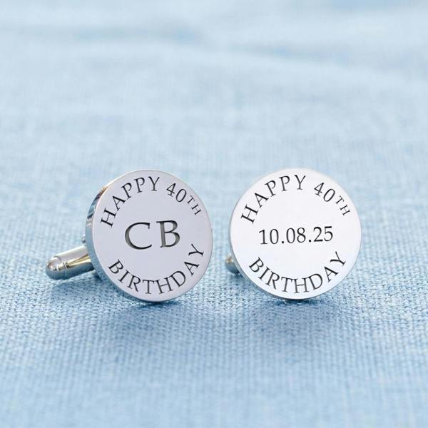 Pair of personalised silver round cufflinks engraved with "CB" and "10.08.25" resting on a textured light blue tablecloth.