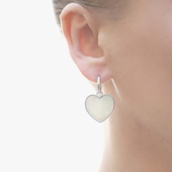 Silver heart charm earrings displayed on an ear.
