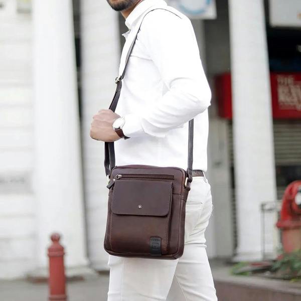 Man wearing a brown leather crossbody bag in an urban setting