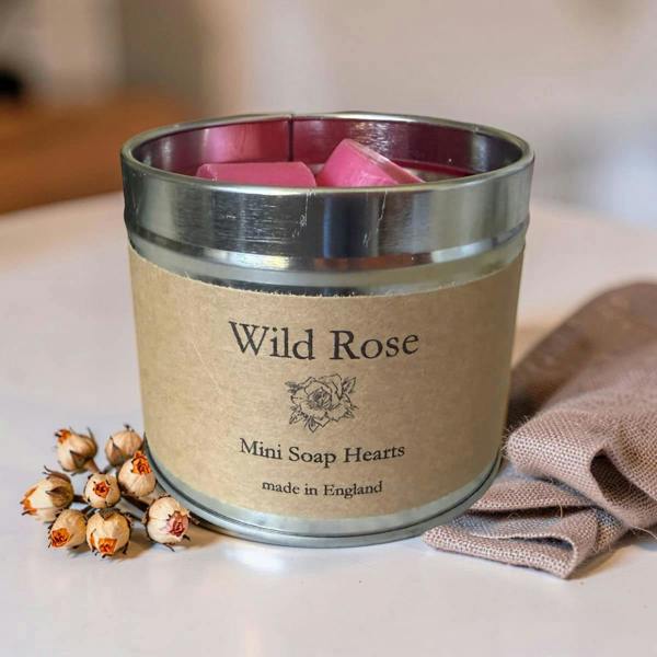 Container of Wild Rose Mini Soap Hearts with flowers and a cloth on a light surface