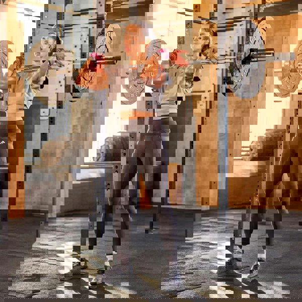 Woman lifting weights in a gym setting wearing  adidas wrist wraps