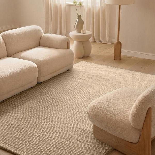 Beige sofa and armchair in a living room with a textured rug and neutral decor.