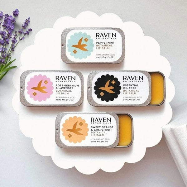 Hydrating Lip Balms set by Scottish Skincare brand Raven Botanicals, displayed on a white riser with a sprig of lavender lying alongside.
