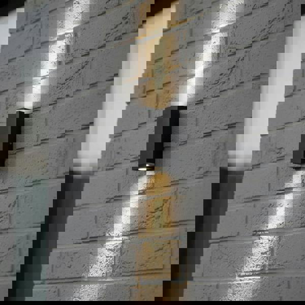 black outdoor up and down wall light mounted on a grey brick wall 