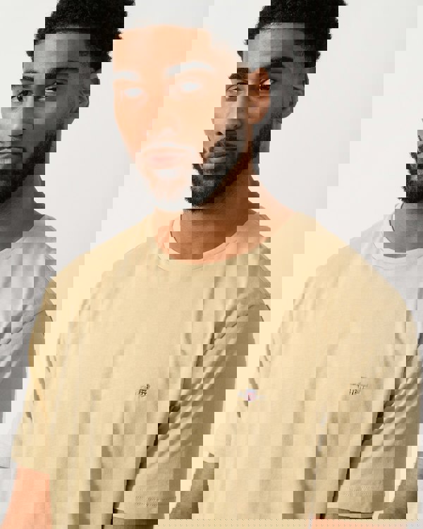 detail shot of a model wearing a GANT Mens Regular Fit Short Sleeve Shield Logo T-Shirt in Oat Beige