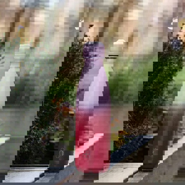 Pink and red water bottle sitting in an urban area