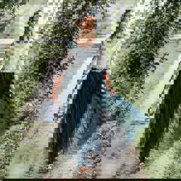 Young girl in a white lace top and blue skirt walking on a path in a garden.