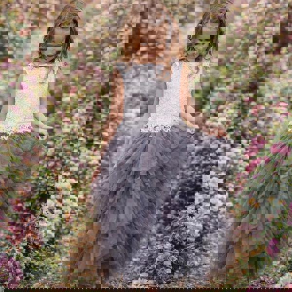 Young girl in a white top and gray tulle skirt standing in a flower garden.