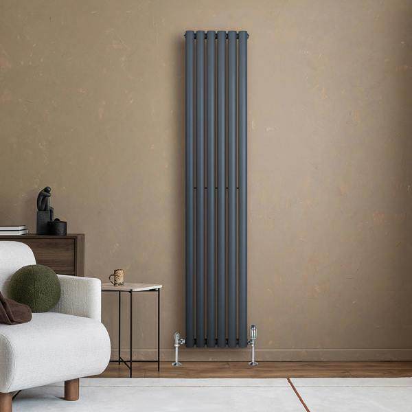 Sleek anthracite grey oval single column radiator standing against a textured beige wall, complemented by modern furniture and decor