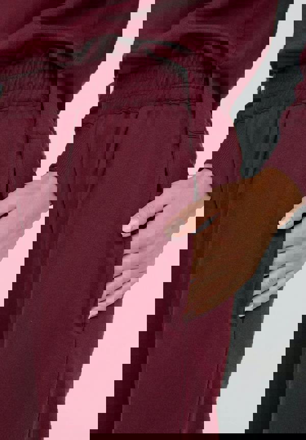 Maroon pants with a hand in the pocket on a light gray background