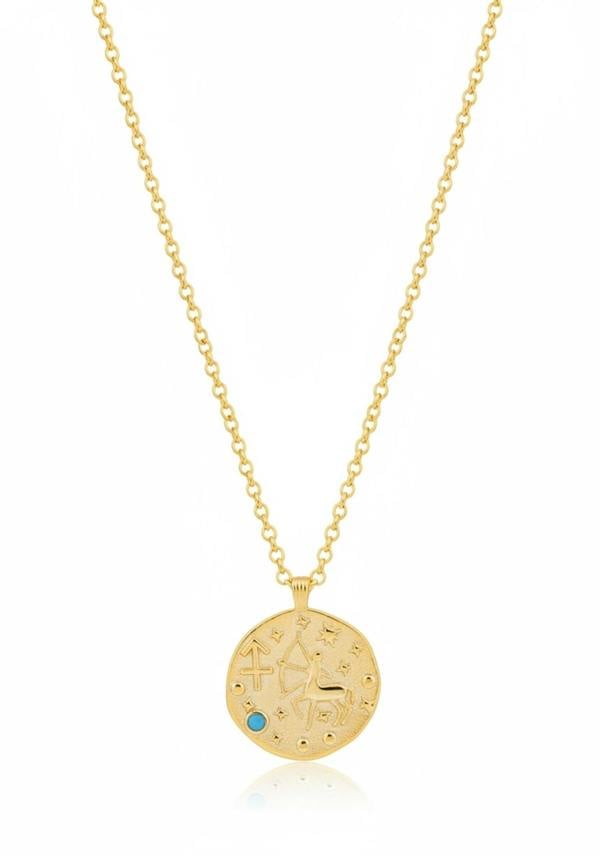 Gold necklace with a circular pendant featuring engraved text and a blue gemstone on a white background.