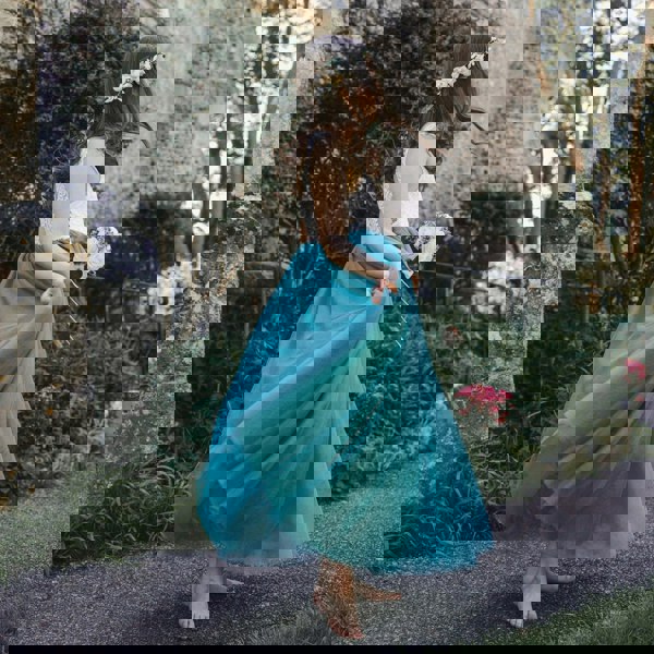 Young girl in a teal blue dress standing in front of a stone building with greenery.