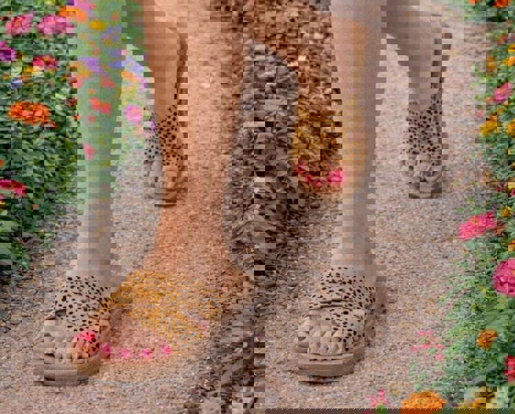 Person wearing leopard print sandals on a pathway with flowers on either side