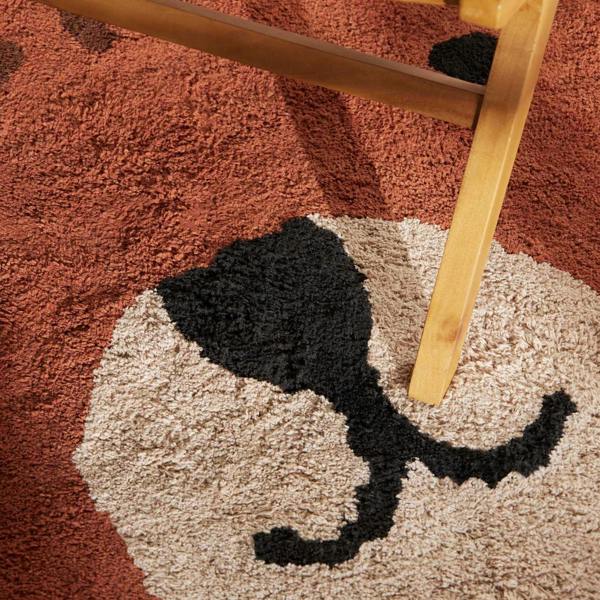 Close-up of a textured rug with a cat design and a wooden chair leg.