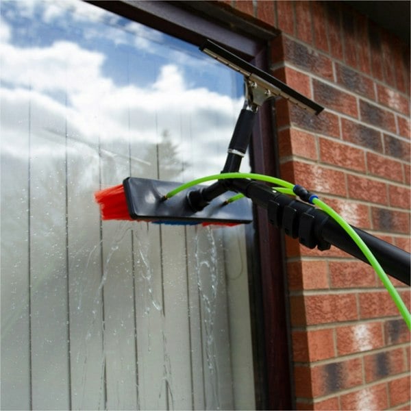 Water fed backpack with 20ft cleaning pole, featuring a squeegee and brush, cleaning a window with a brick wall backdrop