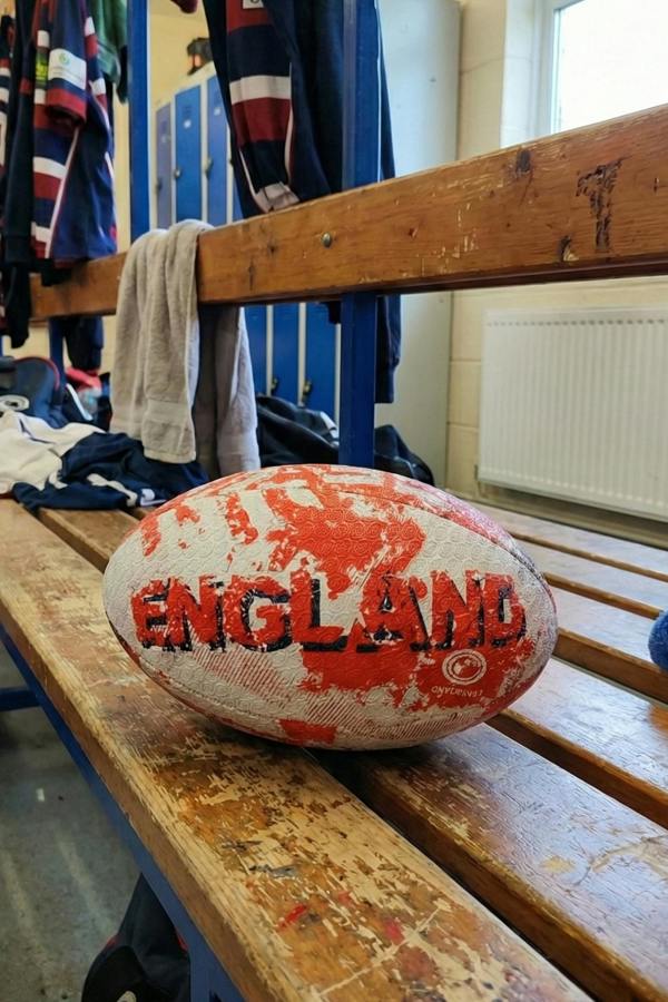 White and red Optimum England rugby ball with ENGLAND print on a wooden changing-room bench - Optimum