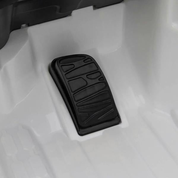 Black accelerator pedal on the white floor panel of a kids electric ride-on car