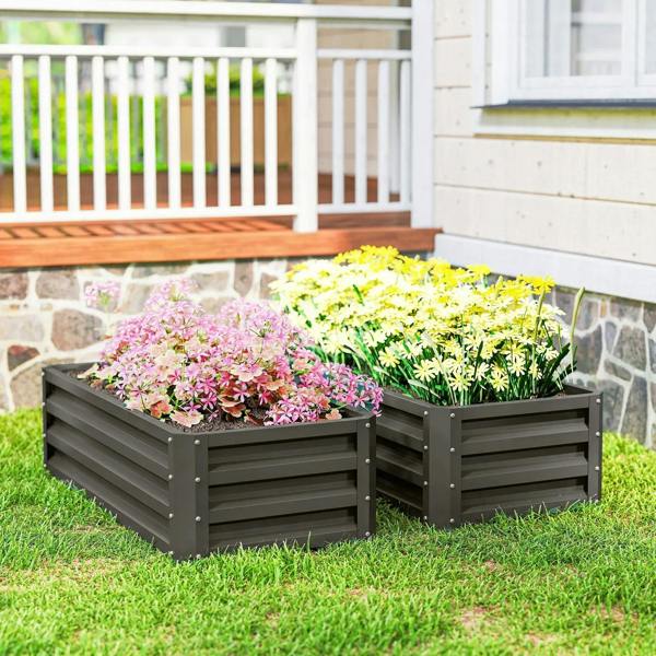 Two dark grey steel planter boxes with pink and yellow flowers in a backyard lawn