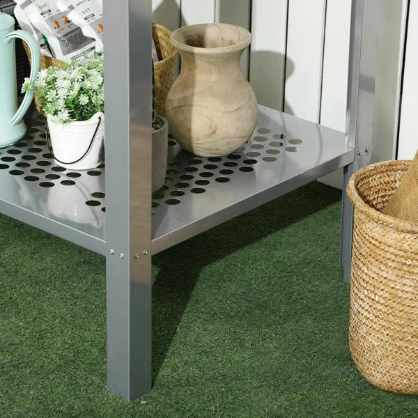 Silver 2-tier plant stand with square legs and perforated shelves, side view near mat.