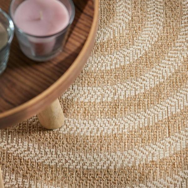 Close-up of a textured beige carpet with a wooden side table and pink candle in the background.