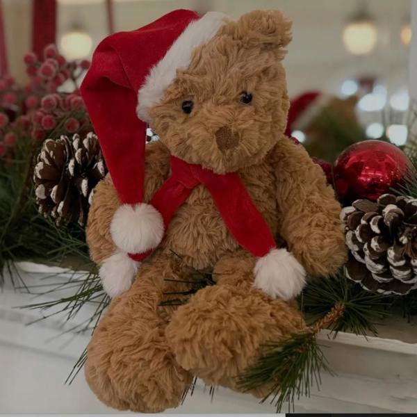 Cuddly Santa Bear plush teddy wearing a red hat and scarf sitting on a decorated festive mantelpiece.