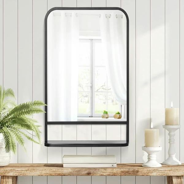 Black wall mirror with storage shelf and rounded frame, mounted above a ledge