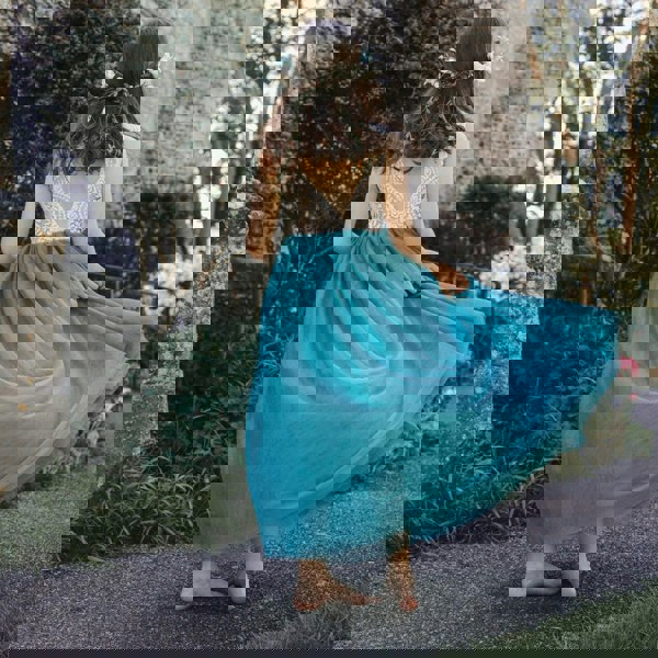 Woman in a turquoise teal dress with a floral headpiece standing in front of a stone building.