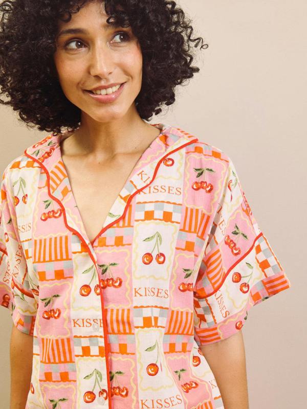 Woman wearing a colorful patterned pyjama shirt with 'Kisses' text and cherry design.
